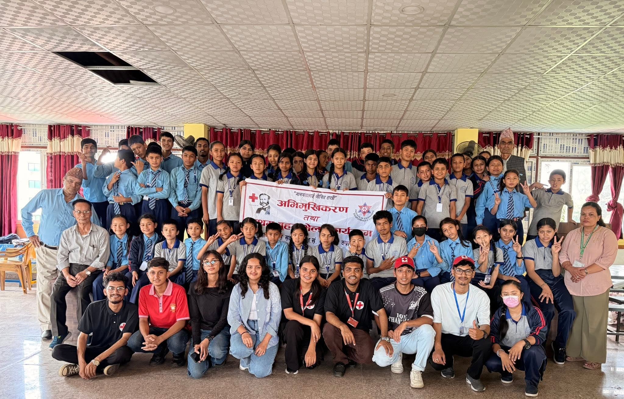 Students in uniform and adults posing for a group photo with a Red Cross banner.
