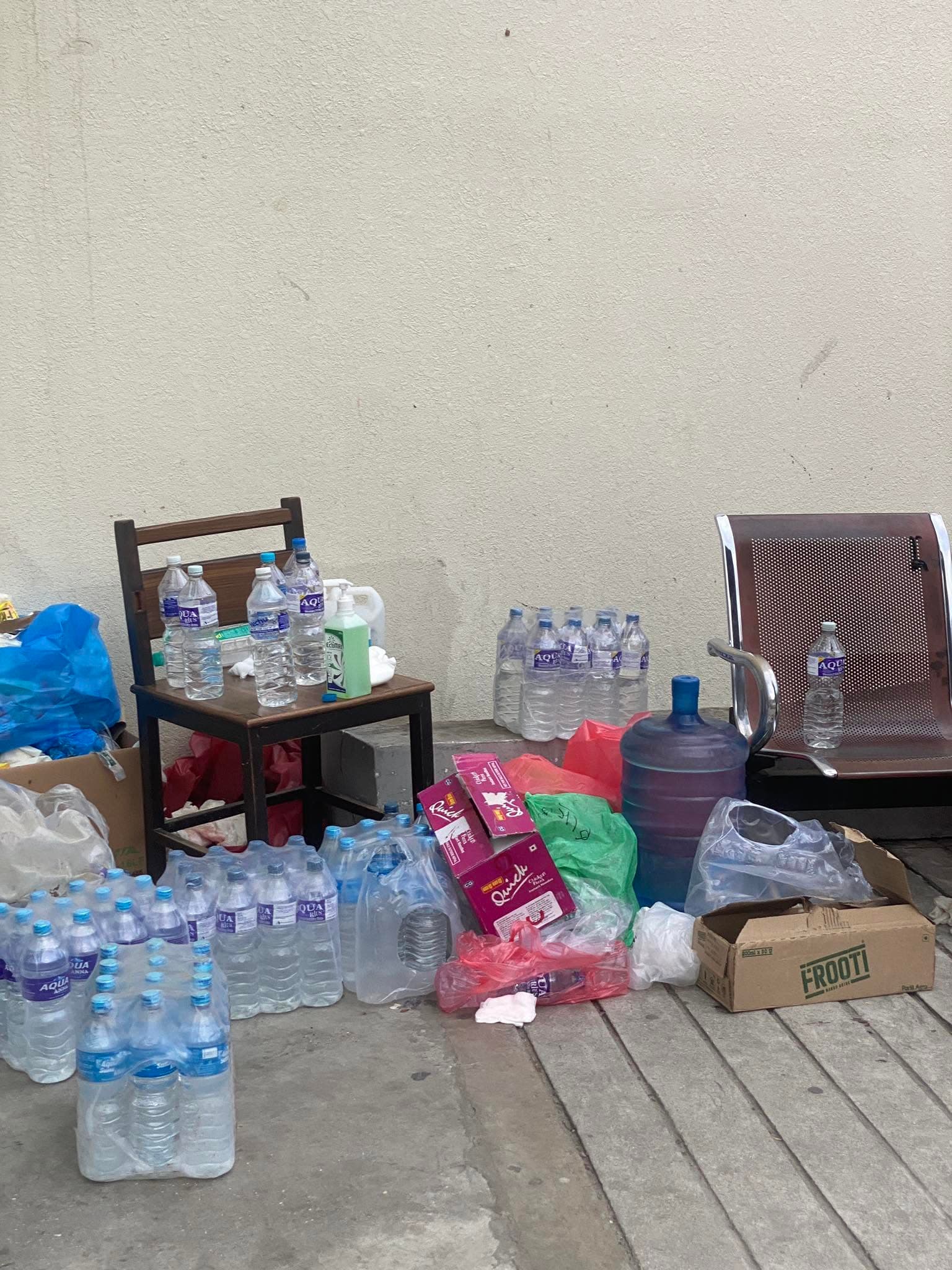 Numerous water bottles, a large jug, and boxes scattered around wooden and metal chairs.