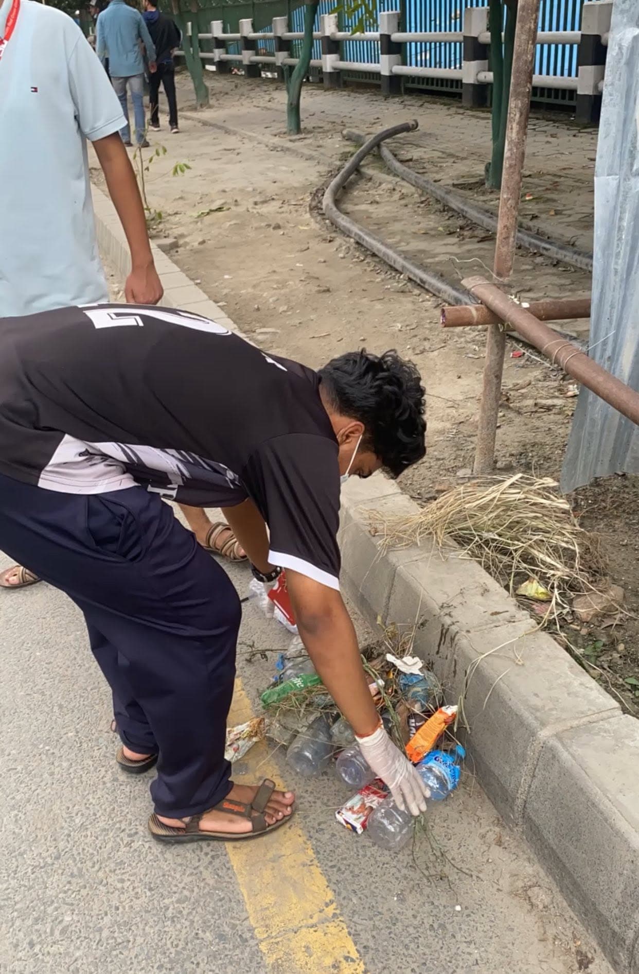 A person wearing a glove picks up plastic bottles and litter from a roadside curb.