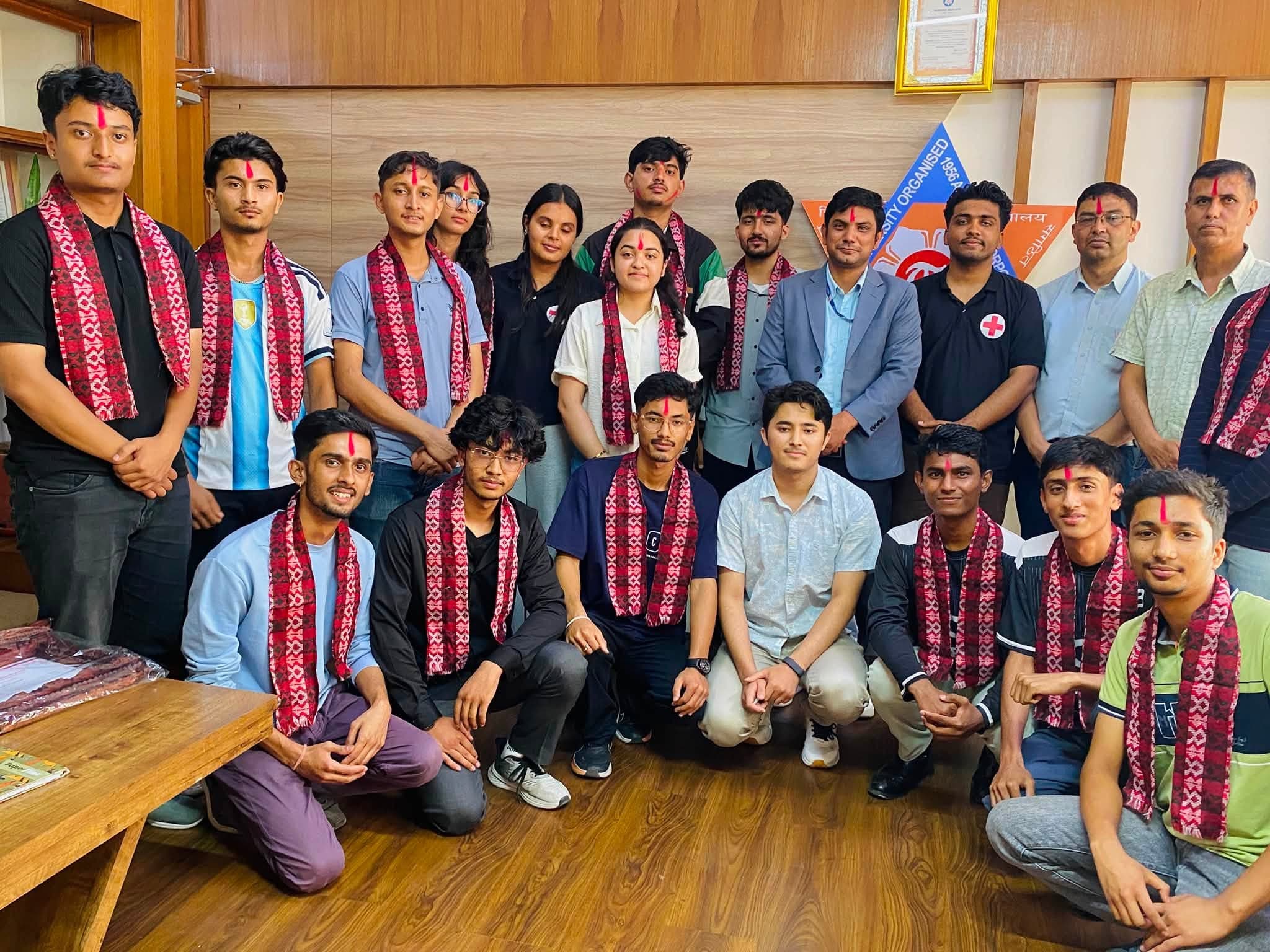 Group of people wearing traditional red patterned scarves and tikas posing for a photo indoors.